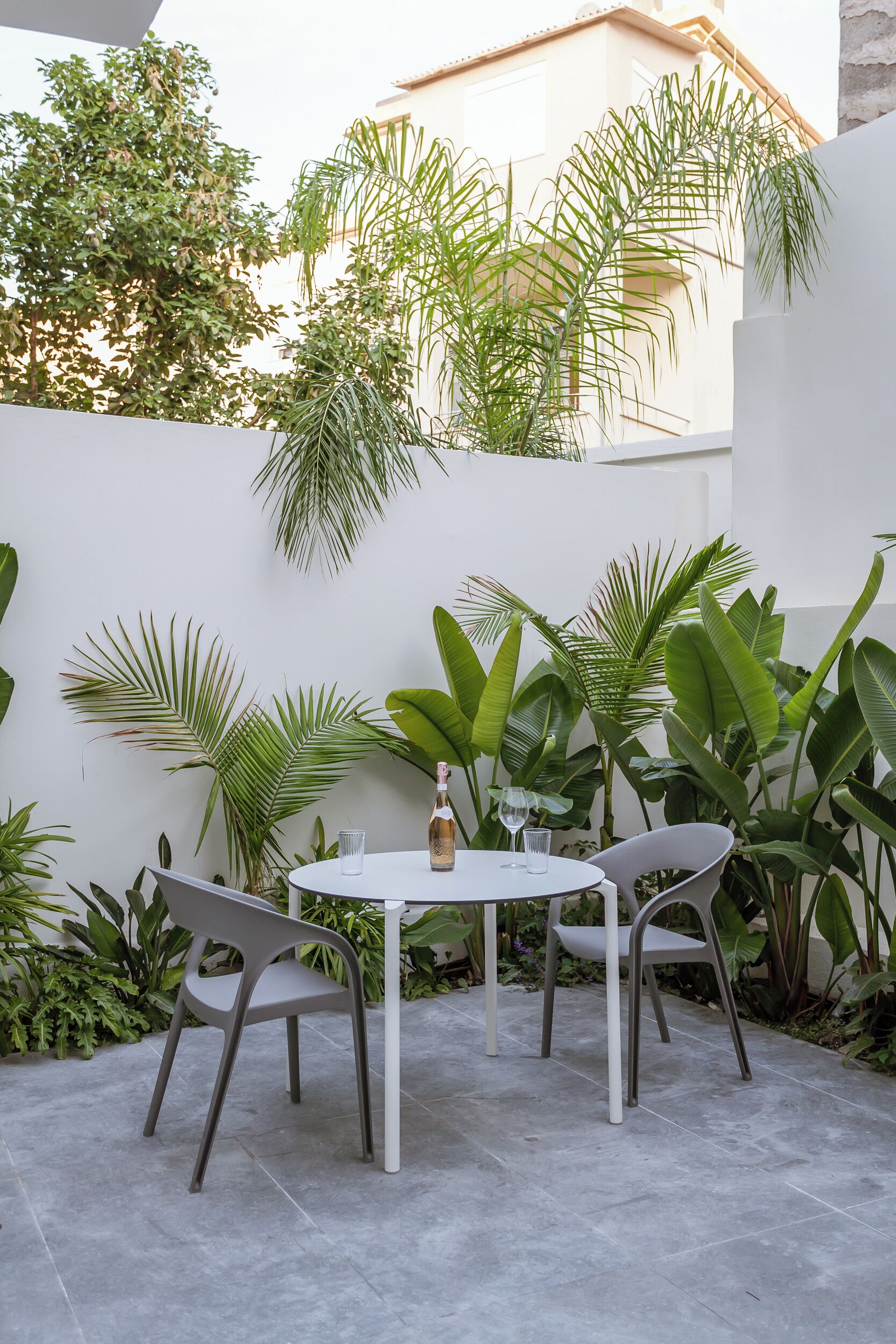 Eine Terrasse mit weißem Tisch und zwei Stühlen, umgeben von üppigen Grünpflanzen und einer weißen Mauer.