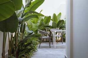 Un couloir étroit avec une table blanche et deux chaises, le tout entouré d’une végétation luxuriante.