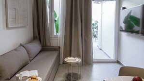 Una sala de estar moderna con un sofá, una mesa de comedor con fruta, y una vista a través de un ventanal.