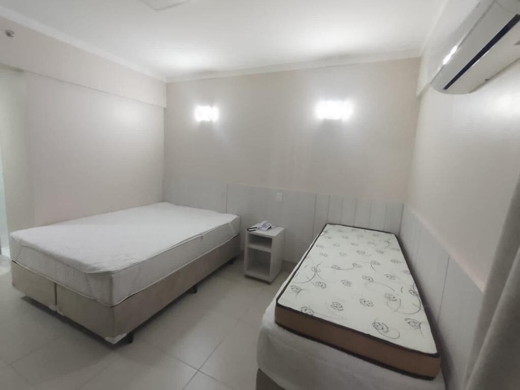 A small, clean room with a bed, a bedside table, and a wall-mounted air conditioner.