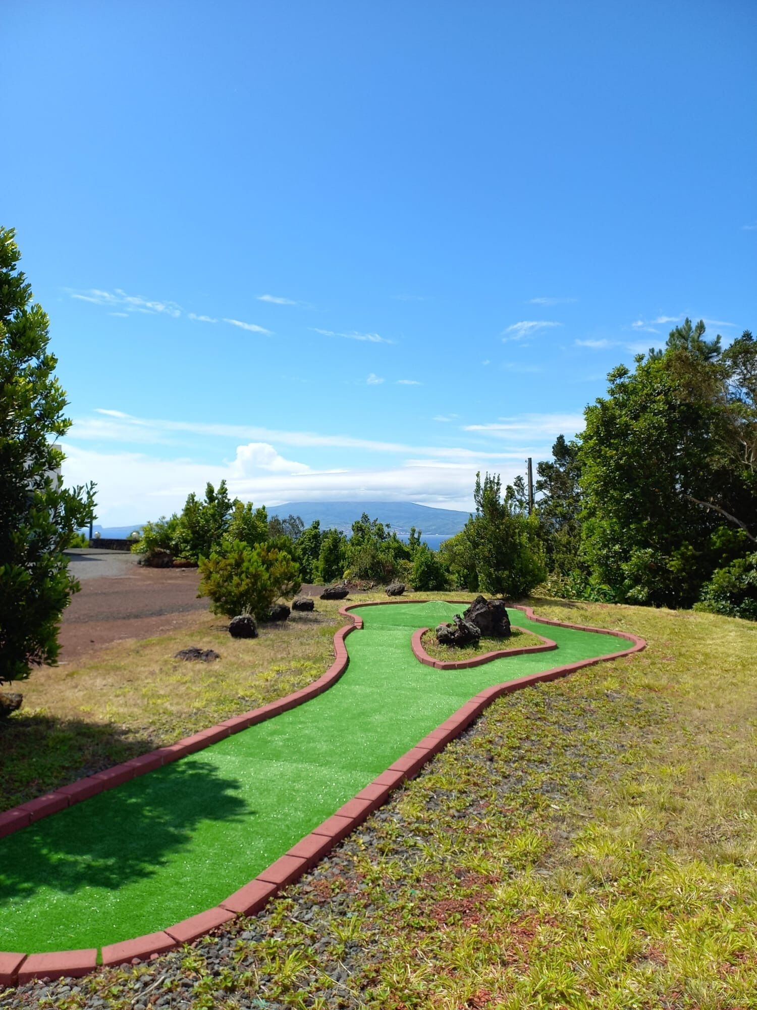 A miniature golf course with a green putting surface, red borders, and natural surroundings.