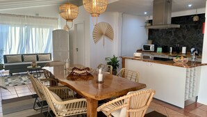 A modern kitchen with a central island, a dining area with wicker chairs, and a living space with a sofa and curtains. - Pico Terrace (Madalena)