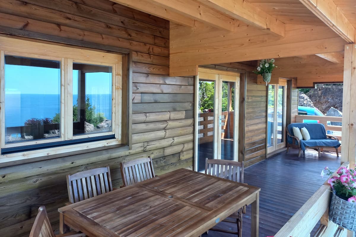 A wooden cabin with a dining area, large windows, and a view of the sea.