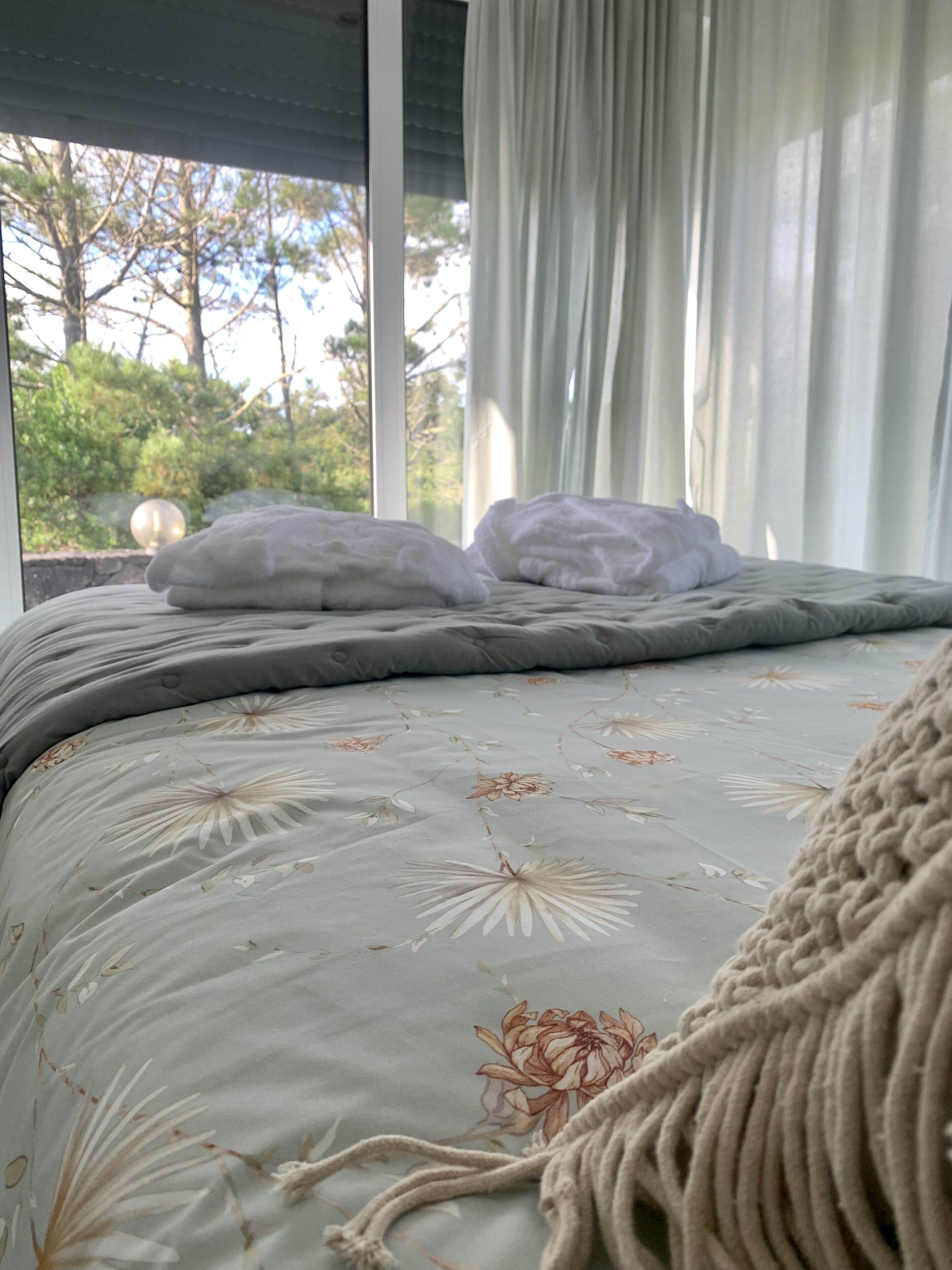 Een bed met een bloemenbedekker, een gebreide plaid en twee kussens.