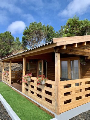 A wooden cabin with a porch, windows, and a small table and chairs. - Pico Terrace (Madalena)