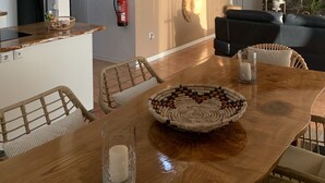 A modern kitchen with a central island, a dining area with a wooden table and woven chairs, and a living area with a black leather sofa. - Pico Terrace (Madalena)