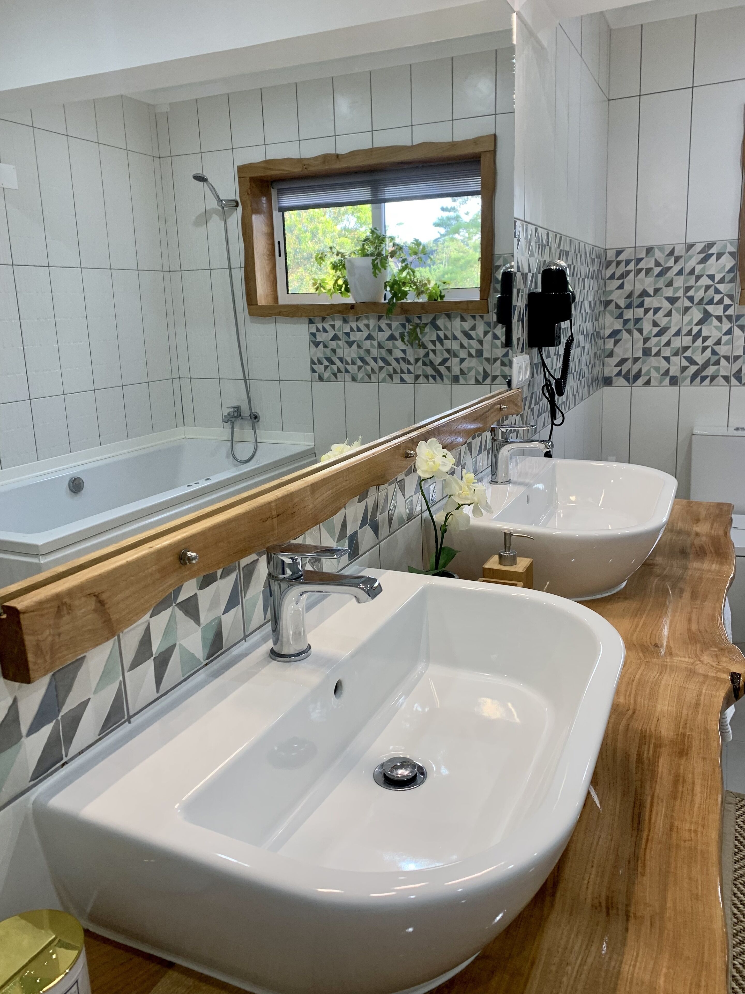 Ein Badezimmer mit zwei Waschbecken, einem großen Spiegel und einem Fenster mit Blick auf Grünflächen.