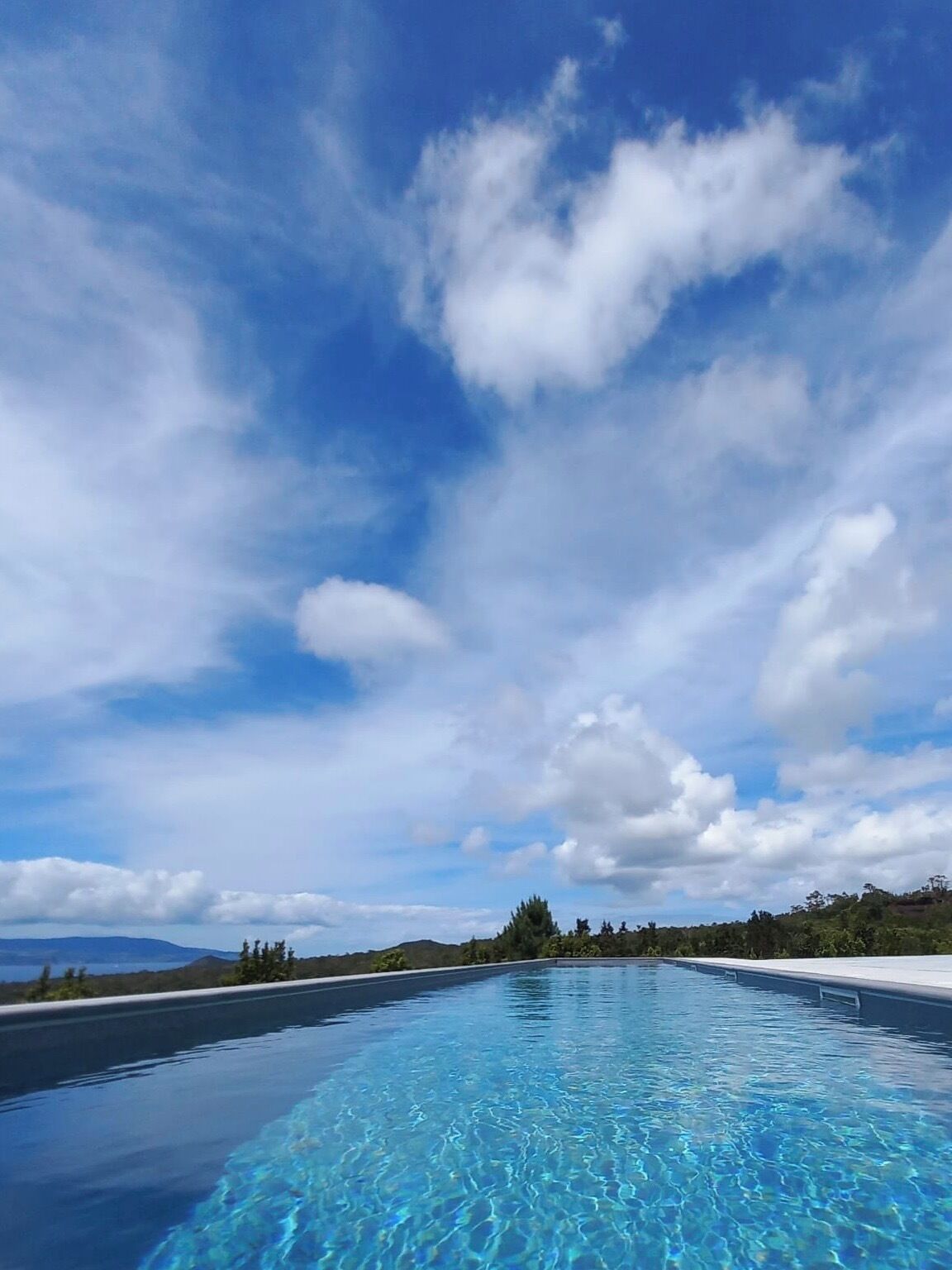 A clear blue sky with clouds above a swimming pool.