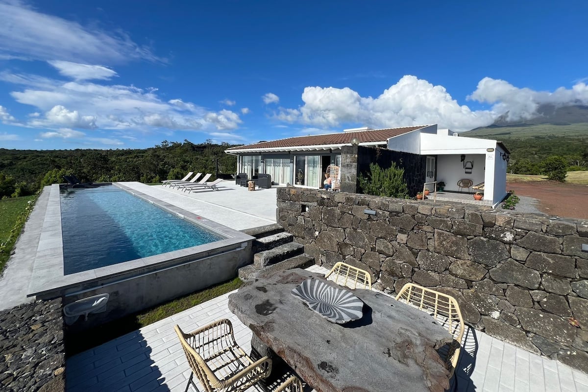 A modern house with a swimming pool, stone wall, and outdoor seating area.