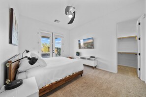 Une chambre à coucher comprenant un lit, des lampes de chevet, un bureau, une chaise, une armoire et un ventilateur de plafond.