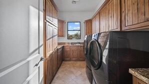 A kitchen with wooden cabinets, a stainless steel washer, and a window with a view of greenery.