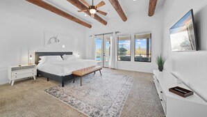A bedroom with a bed, bedside tables, a bench, a ceiling fan, and a large window with a view.