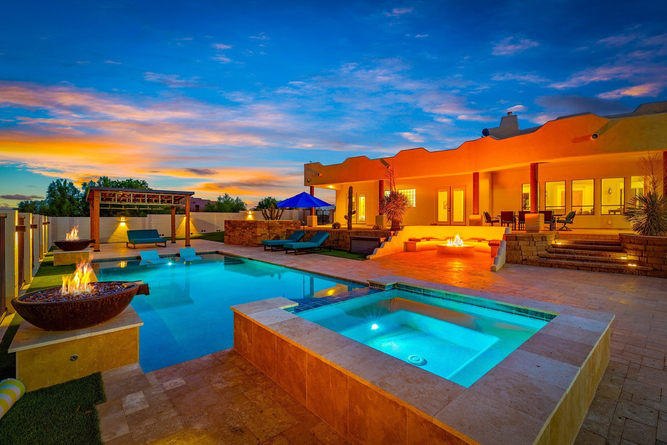 A modern outdoor pool area with a hot tub, lounge chairs, and a covered seating area.