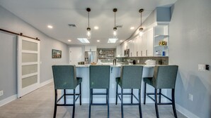 Una cocina moderna con una isla central, taburetes de bar e iluminación colgante.