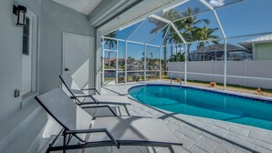 Una piscina con agua azul cristalina, rodeada por un deck blanco y sillones de descanso.