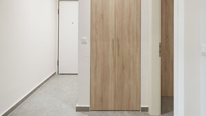 Un couloir avec une porte en bois, des murs blancs et un sol carrelé.