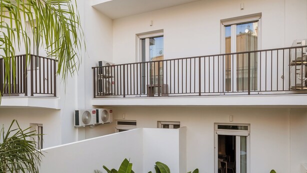 Une terrasse extérieure à plusieurs niveaux, avec une table et des chaises blanches, entourée d’une végétation luxuriante.