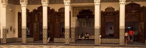 Une cour intérieure agrémentée d’arcs et de colonnes richement décorés, d’un sol carrelé et de quelques personnes.