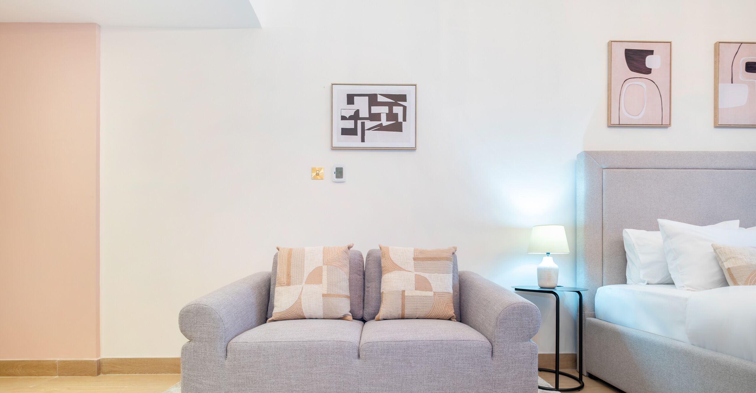 A modern hotel room with a grey sofa, a bed with white bedding, and abstract art on the walls.