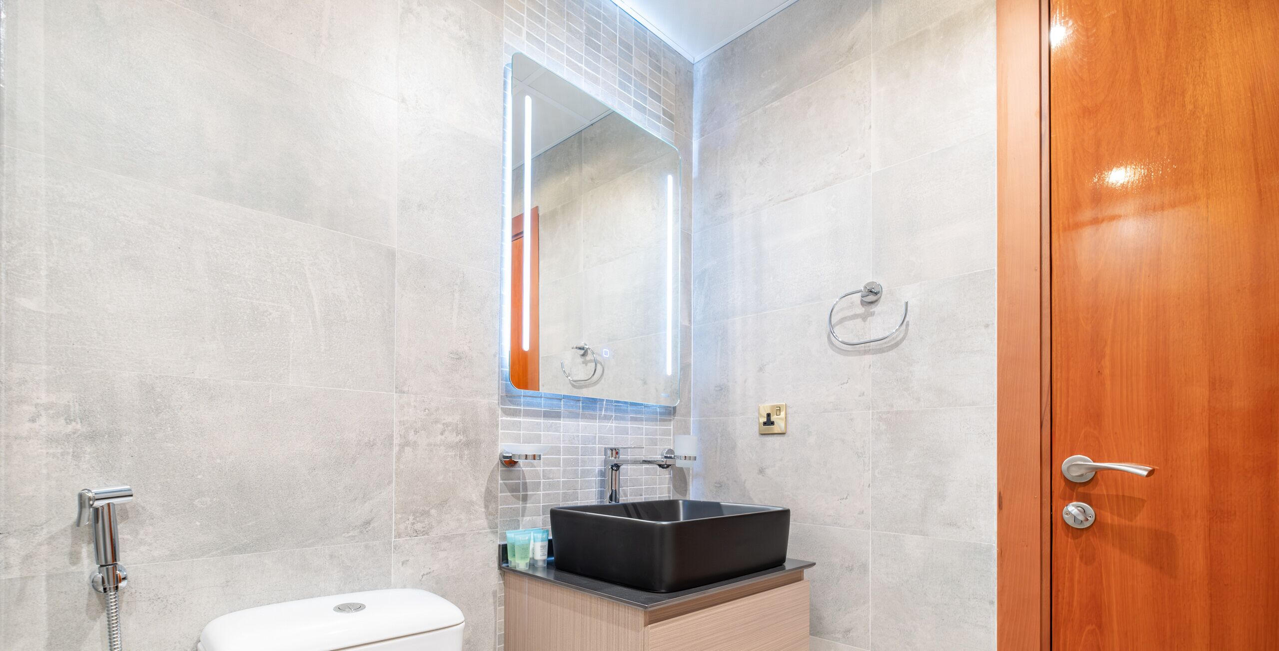 A modern bathroom with a large mirror, a black sink, and a wooden door.