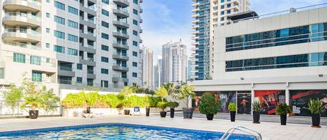 A modern urban setting with a swimming pool, potted plants, and high-rise buildings in the background.
