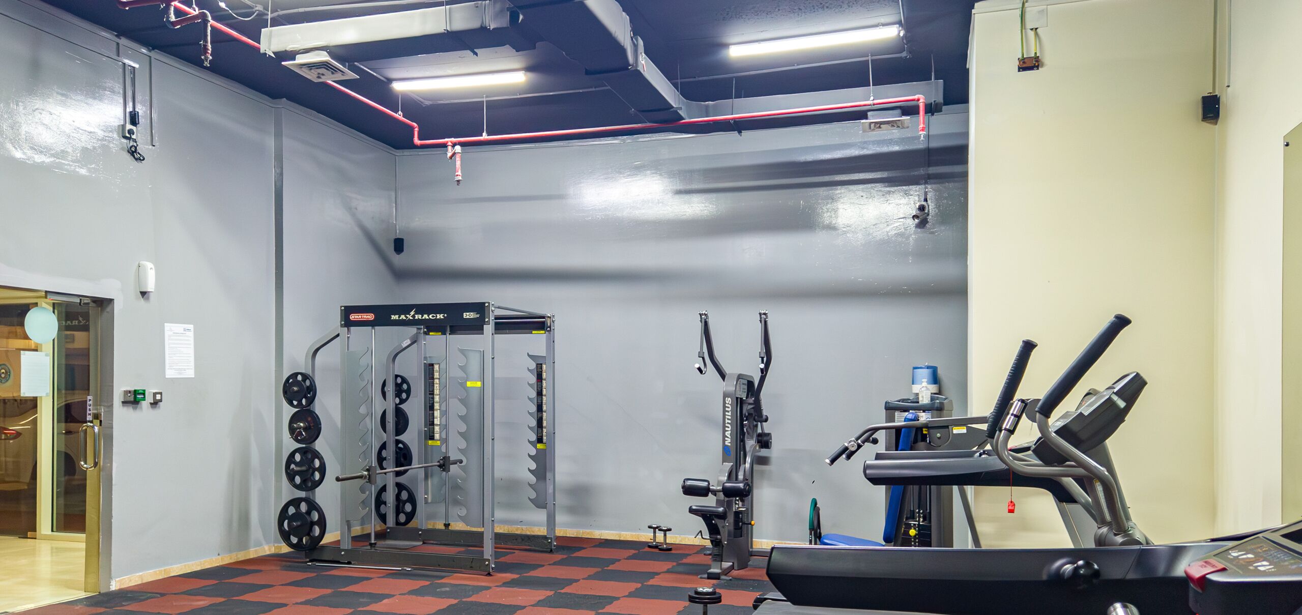 A gym with weightlifting equipment, a treadmill, and a wall-mounted squat rack.