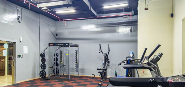 A gym with weightlifting equipment, a treadmill, and a wall-mounted squat rack. - LUX  The Marina View Suite 1 (Dubai)