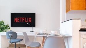 Eine moderne Küche mit Waschmaschine, einem Esstisch mit Stühlen und einem an der Wand befestigten Fernseher, der "NETFLIX" zeigt.