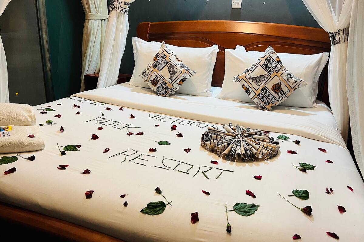 A neatly made bed with a decorative pillow, a rose petal arrangement, and a towel on the side.