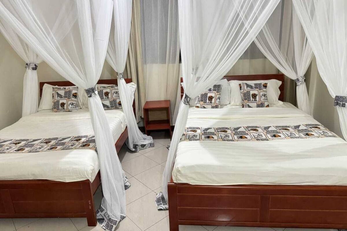 A room with two beds, each with a canopy. There is a small table between the beds.