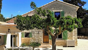 Una casa de piedra con un árbol en el frente, un patio con mesa y sillas, y una puerta de madera.