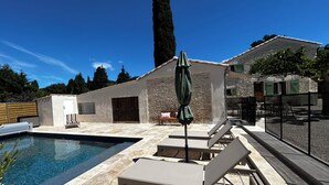 Piscina con sillas de descanso y una sombrilla, rodeada de muros de piedra y una valla de madera.