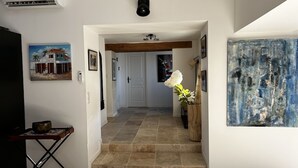 Un pasillo con suelo de baldosas, viga de techo de madera, una puerta blanca y un cuadro en la pared.