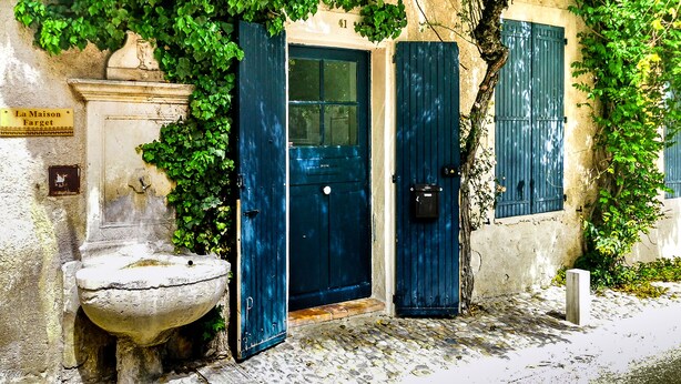 Un edificio con una puerta azul, una fuente de piedra y un letrero que dice "La Maison Farget".