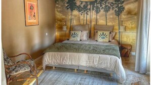 Un dormitorio con una cama, una silla, un mural en la pared y una lámpara colgante.