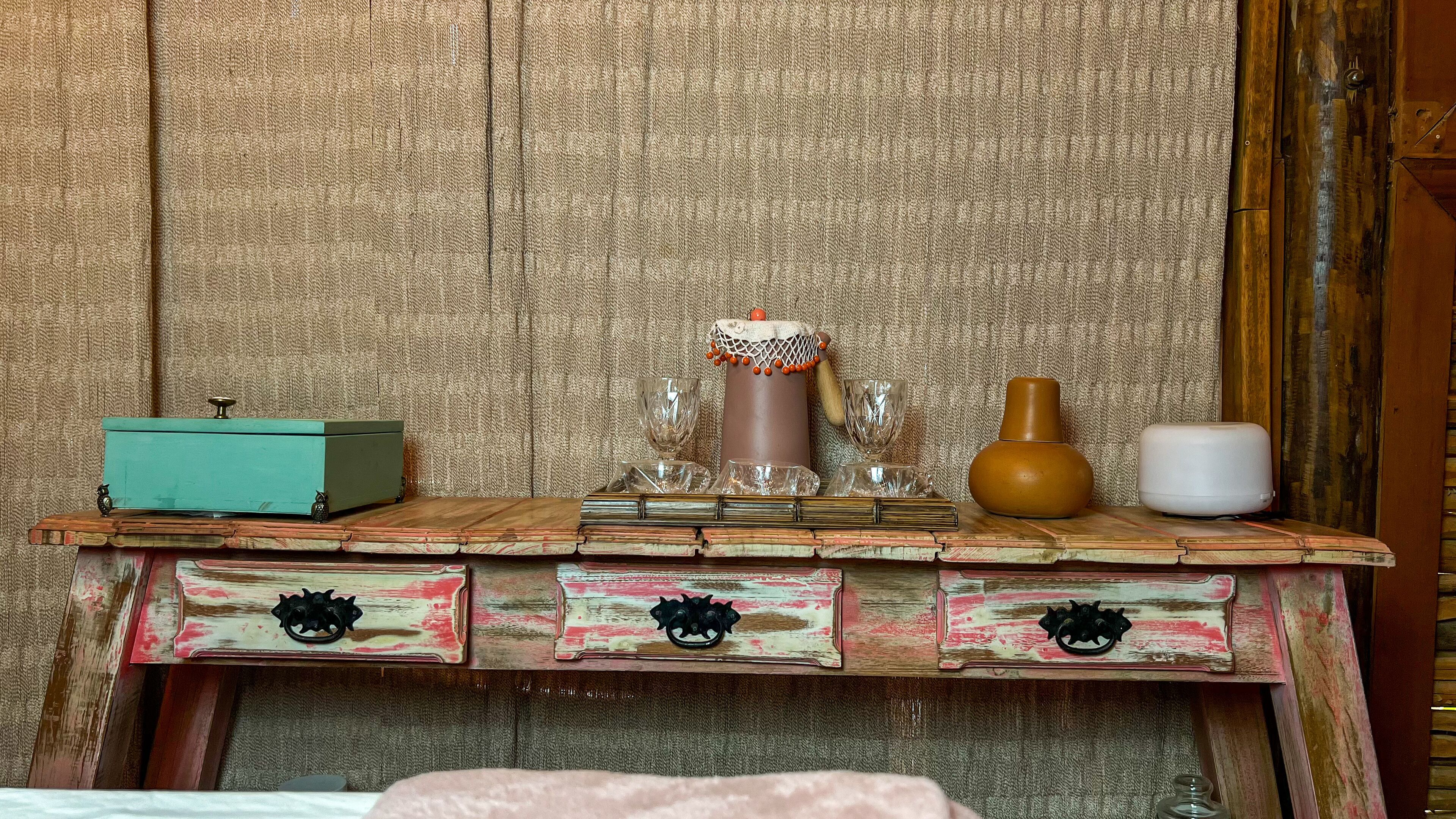 Una mesa de madera rústica con un estilo vintage, que incluye un cofre azul verdoso, una vela decorativa y un florero.