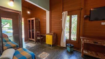 Una cabaña de madera con una cama, un pequeño armario amarillo, una silla y una ventana con cortinas.