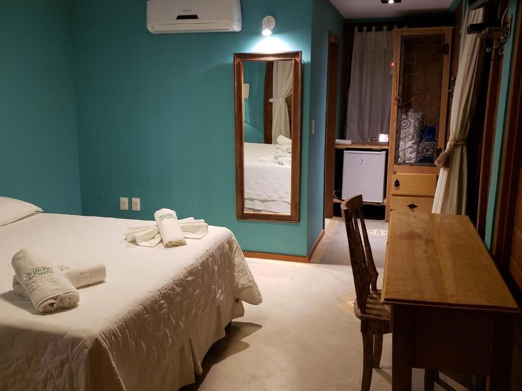 A hotel room with a bed, a wooden desk, a mirror, and a wardrobe.