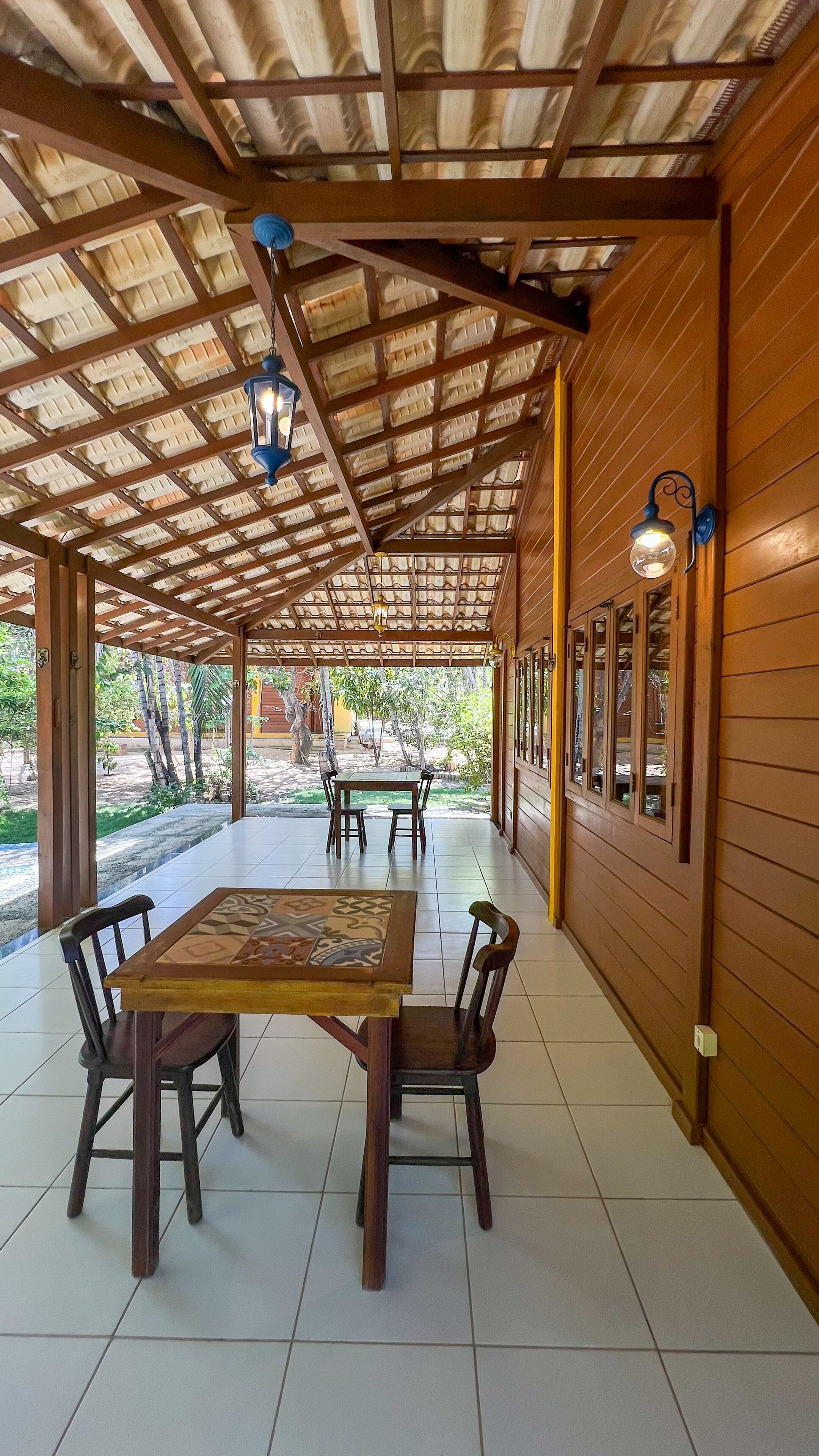 Un patio cubierto con mesa y sillas de madera, piso de baldosas y vistas al jardín.