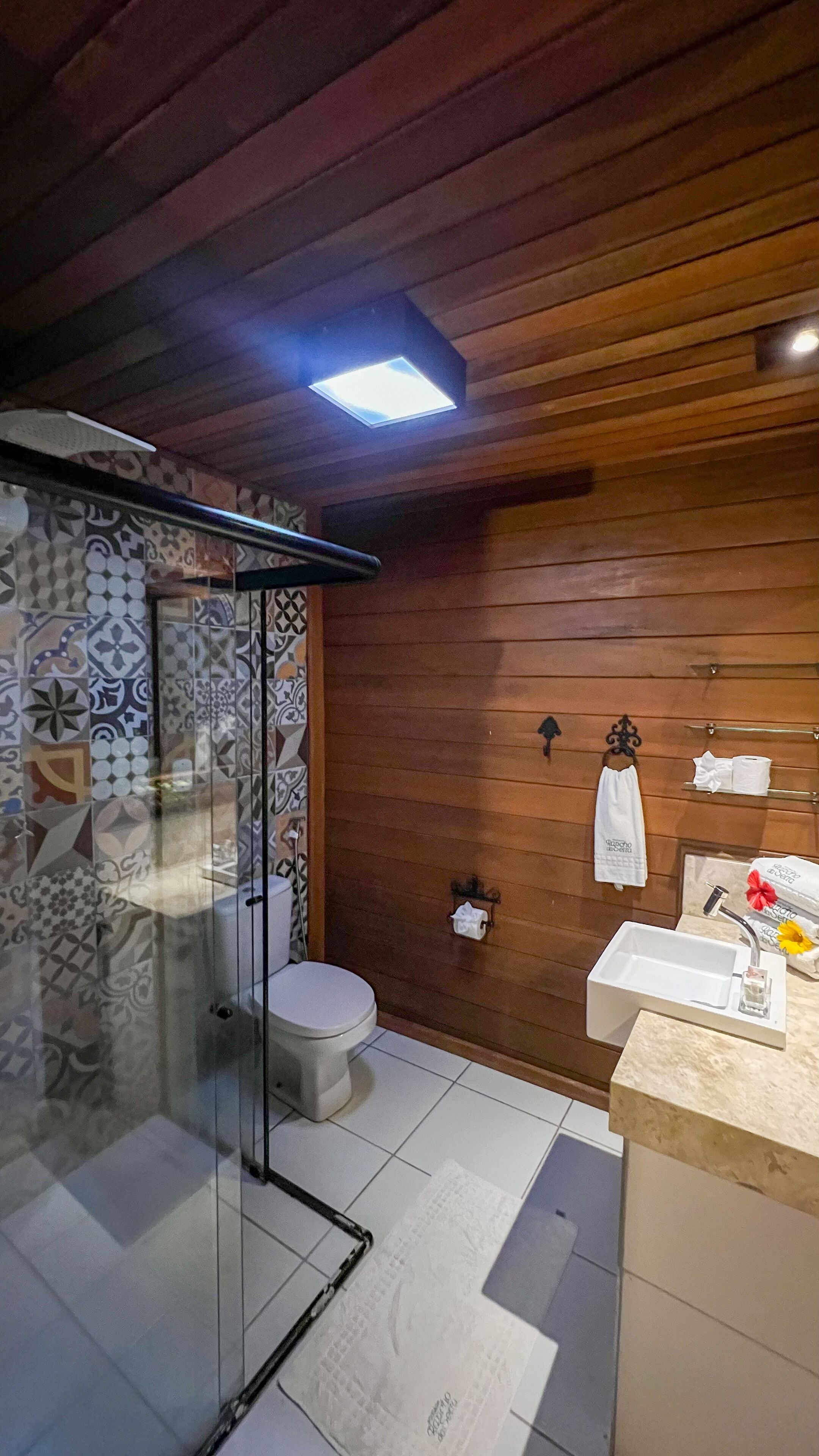 Une salle de bain avec un plafond en bois, une cabine de douche en verre, des toilettes, un lavabo avec un miroir et un porte-serviettes.