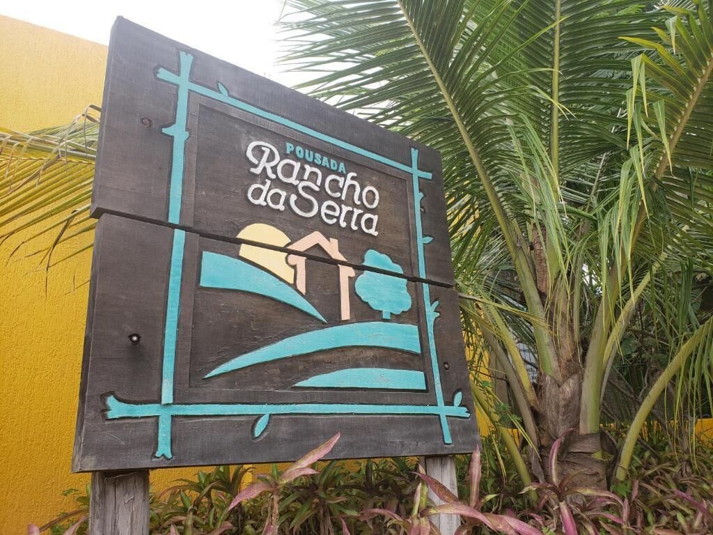 Un cartello in legno con il testo "Pousada Rancho da Serra" e un disegno stilizzato di un paesaggio.