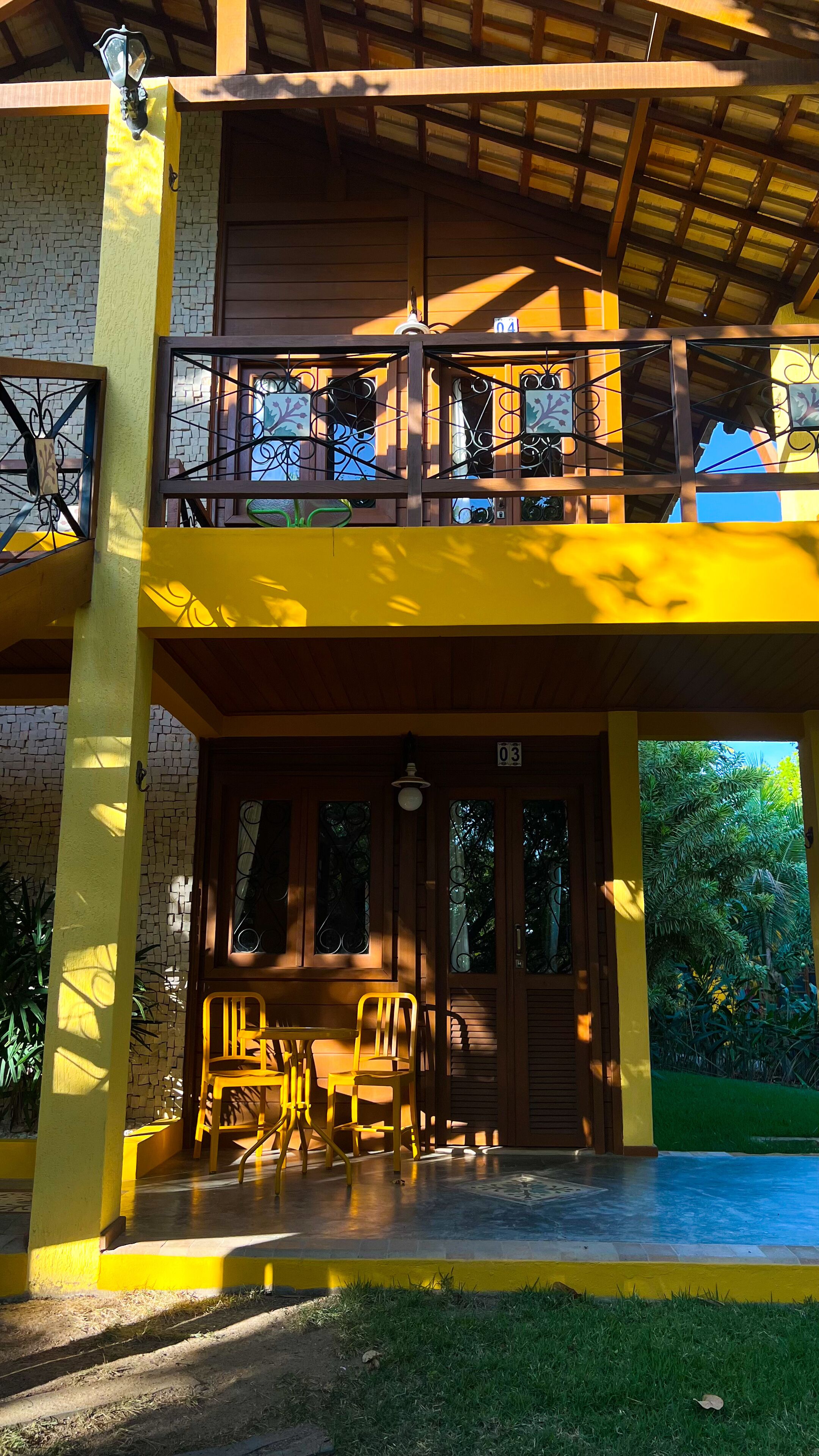 A two-story building with a balcony, a covered patio area with chairs, and a number sign indicating room or unit number.