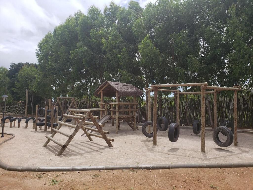A playground with wooden structures, tire swings, and a small hut.