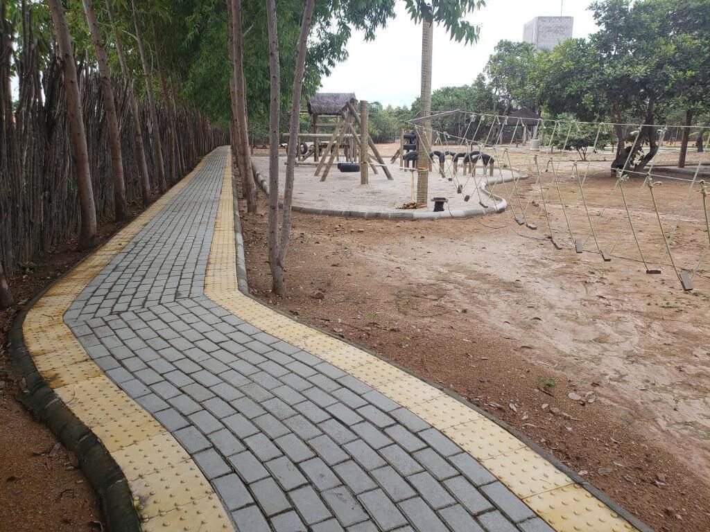 A paved pathway with tactile paving for the visually impaired, surrounded by trees and a playground area.