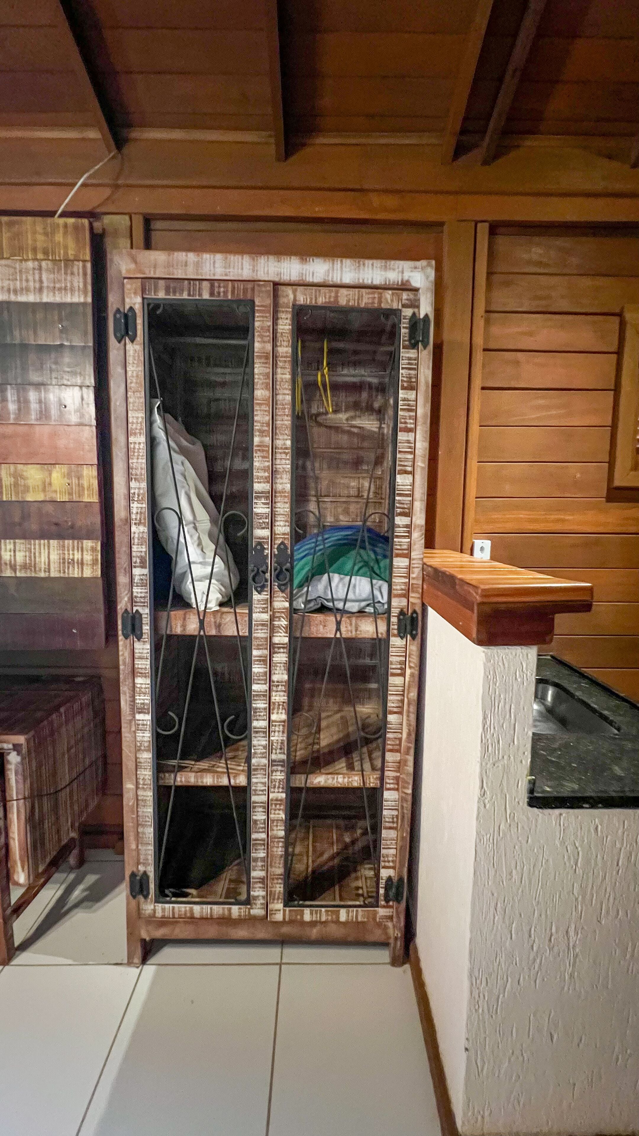 A room with a wooden wardrobe, a small wooden bench, and a white tiled floor.
