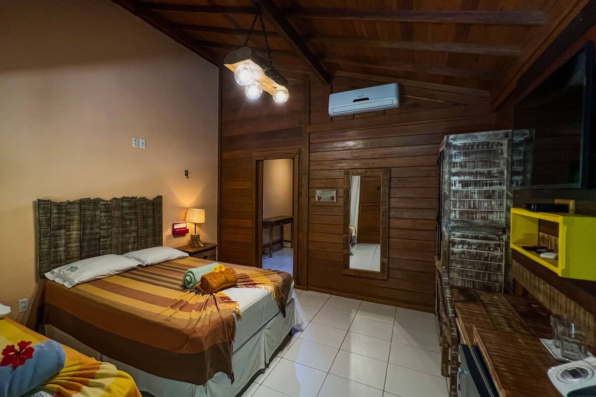 A room with two beds, a wooden ceiling, a small table with a lamp, and a mirror on the wall.