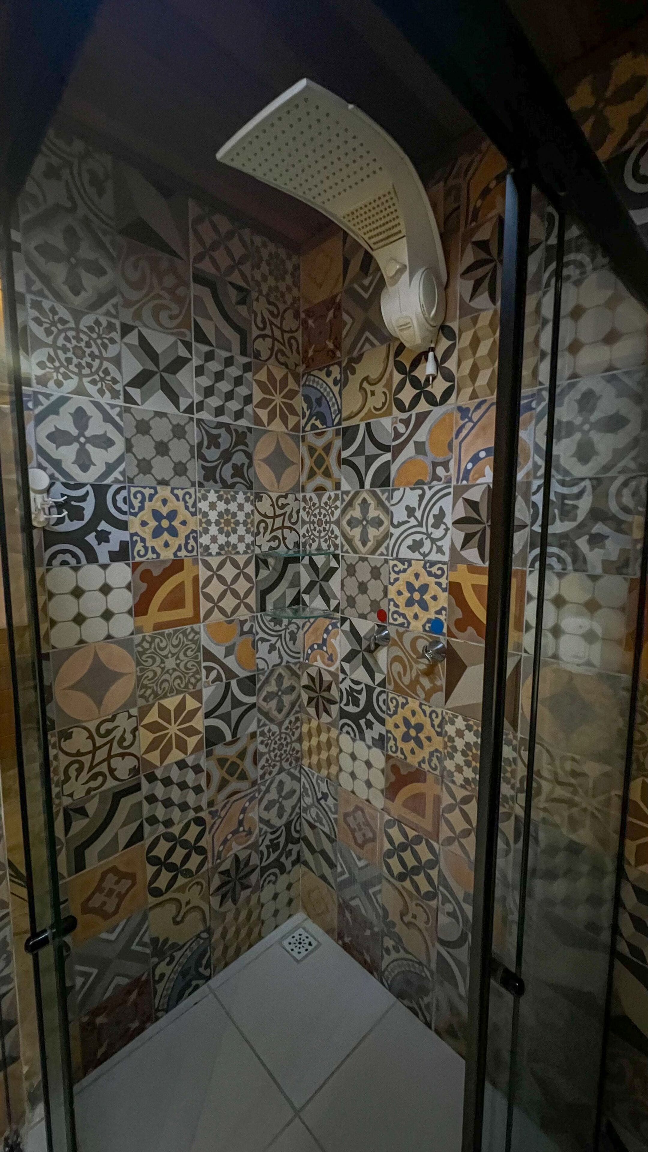 A shower with a white ceiling and a variety of patterned tiles on the walls.