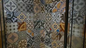 A shower with a white ceiling and a variety of patterned tiles on the walls.