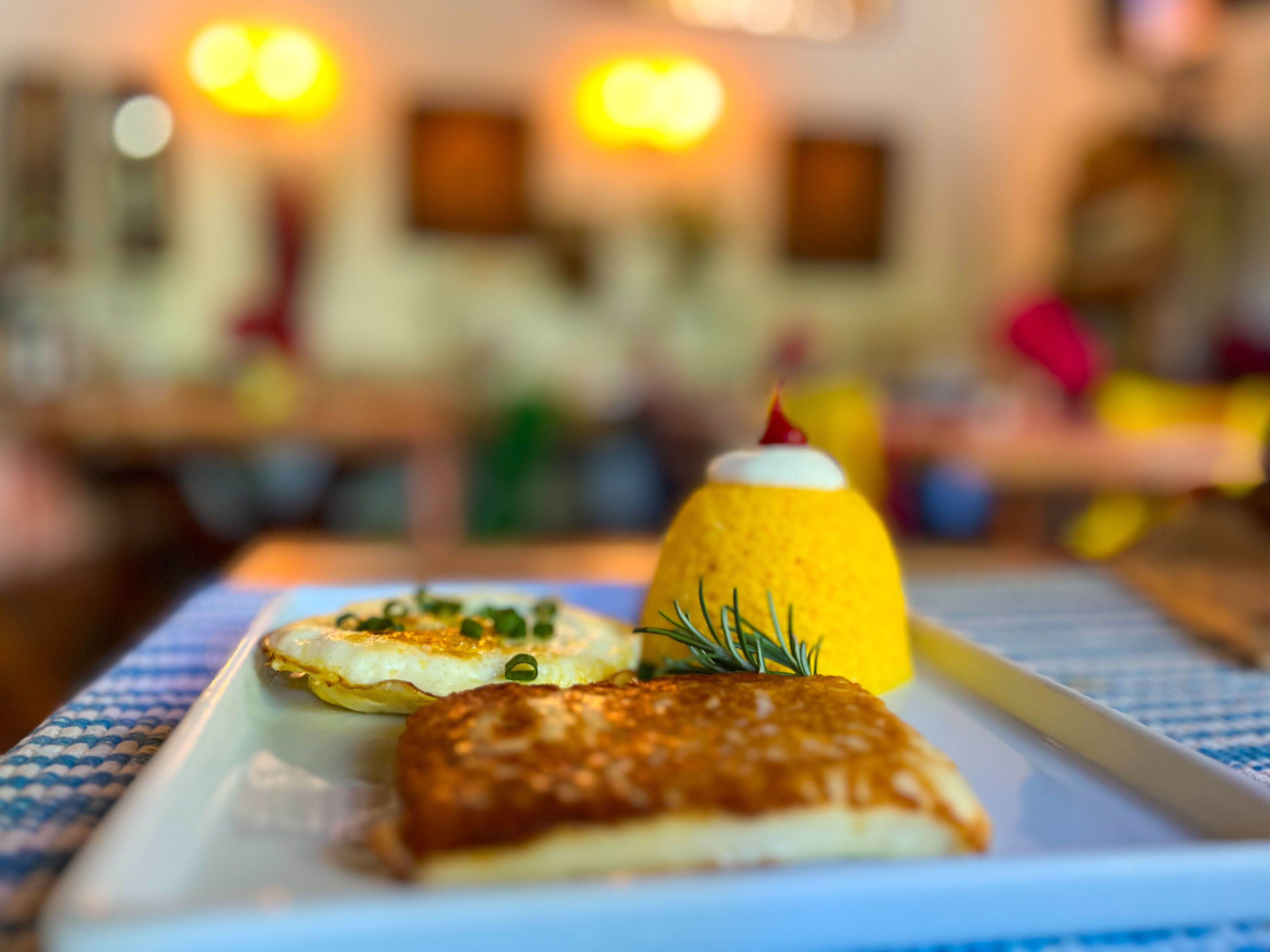 A plate with a yellow cone-shaped food item, a pancake, and a piece of bread.