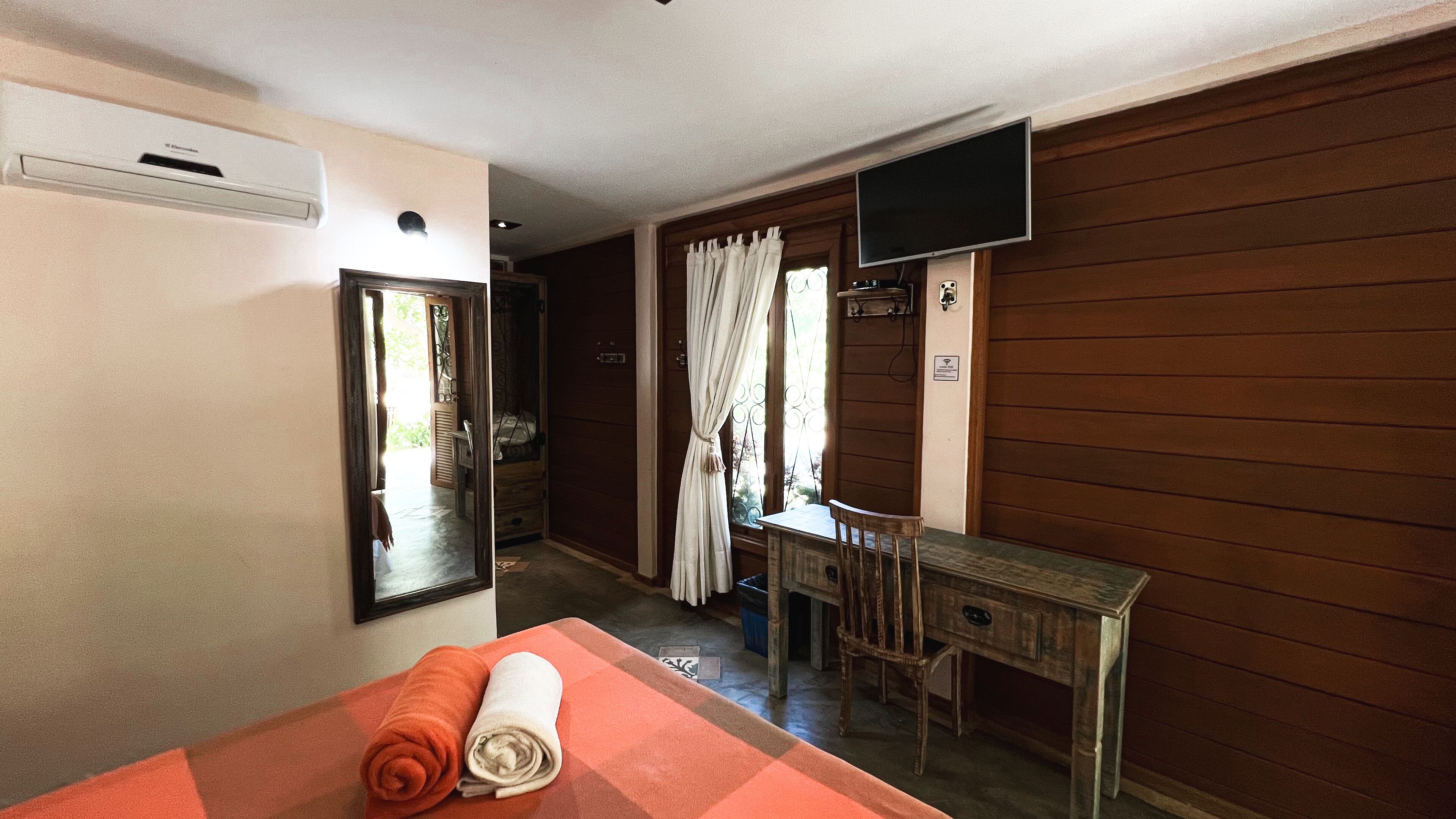 A room with a bed, a desk, a television, and a window with curtains.